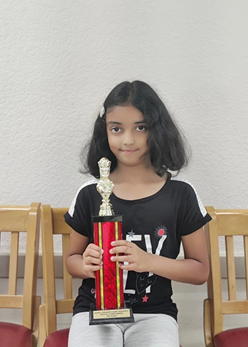 A proud Time2Chess student holding her trophy after consistent chess training and practice.